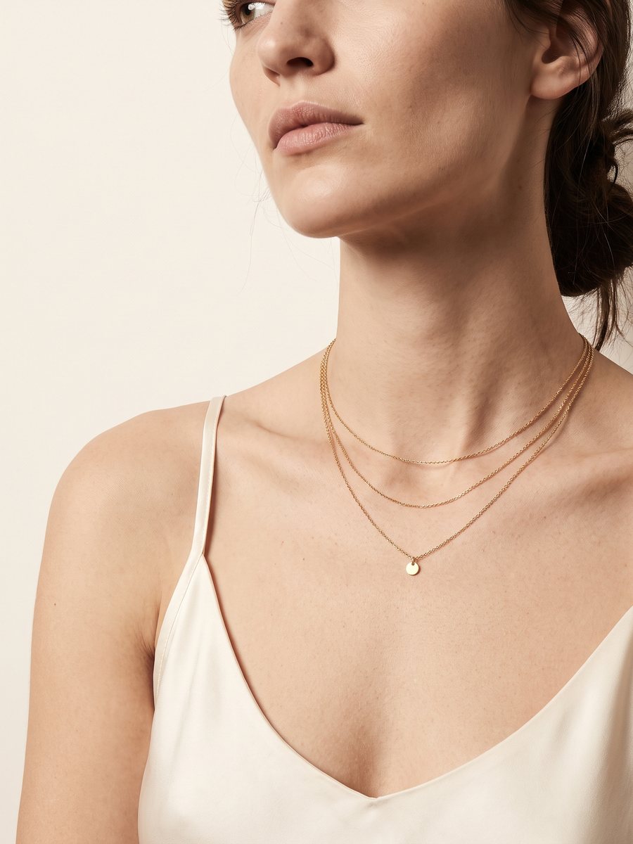 Hals en sleutelbeen van een model met dezelfde drie fijne gouden kettinkjes, het hangertje op de blote huid boven een ivoorkleurig hemdje