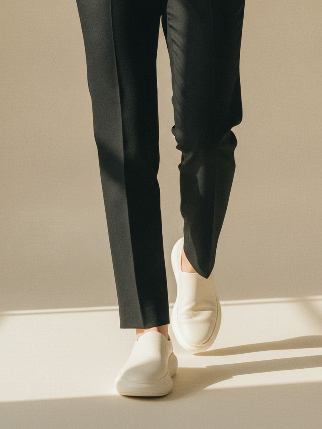 Benen van iemand die naar de camera loopt op gebroken witte leren sneakers bij een zwarte pantalon