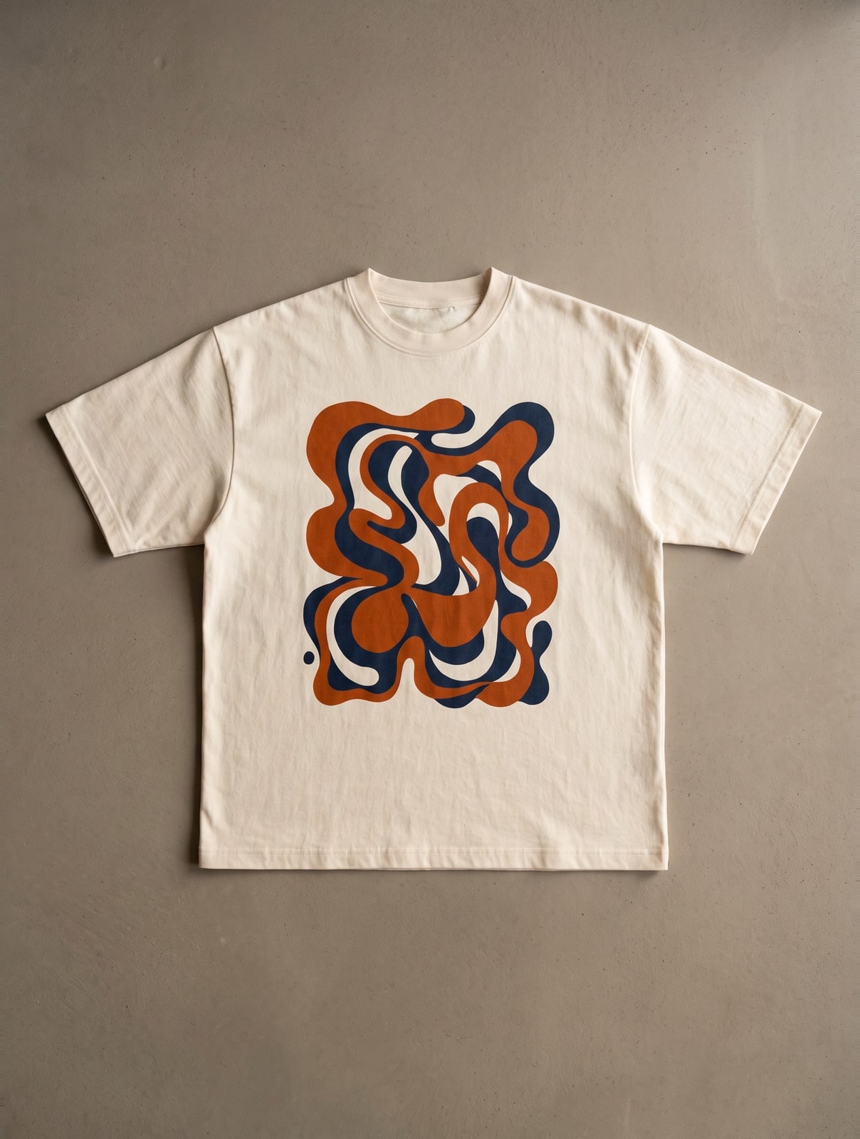 Ecru T-shirt met een abstracte grafische print in oranje en donkerblauw, platgelegd op een grijze ondergrond